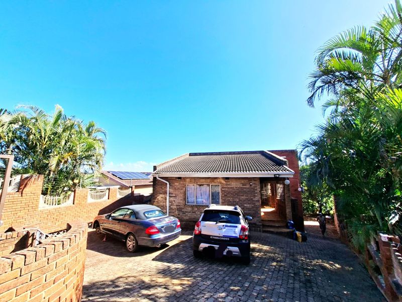 Front view of a face-brick residential house featuring a paved driveway, tiled roof, and perimeter brick walling with security fencing.