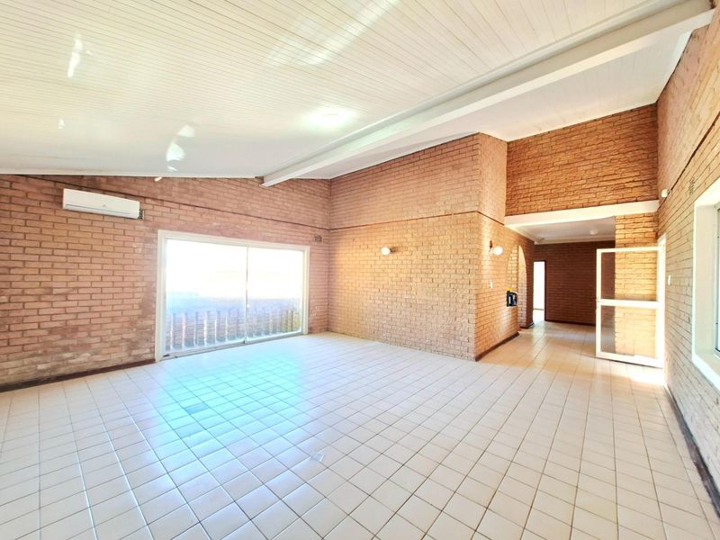 Spacious open-plan living area featuring exposed brick walls, white timber-paneled ceilings, tiled flooring, and a wall-mounted air conditioning unit.