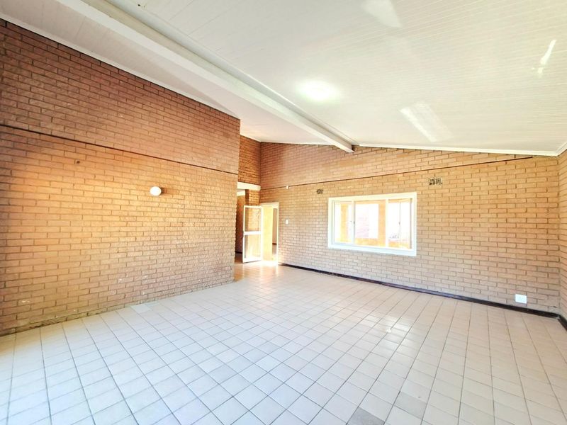 A spacious, empty living area featuring exposed brick walls, tiled flooring, and a high raked ceiling with exposed beams.