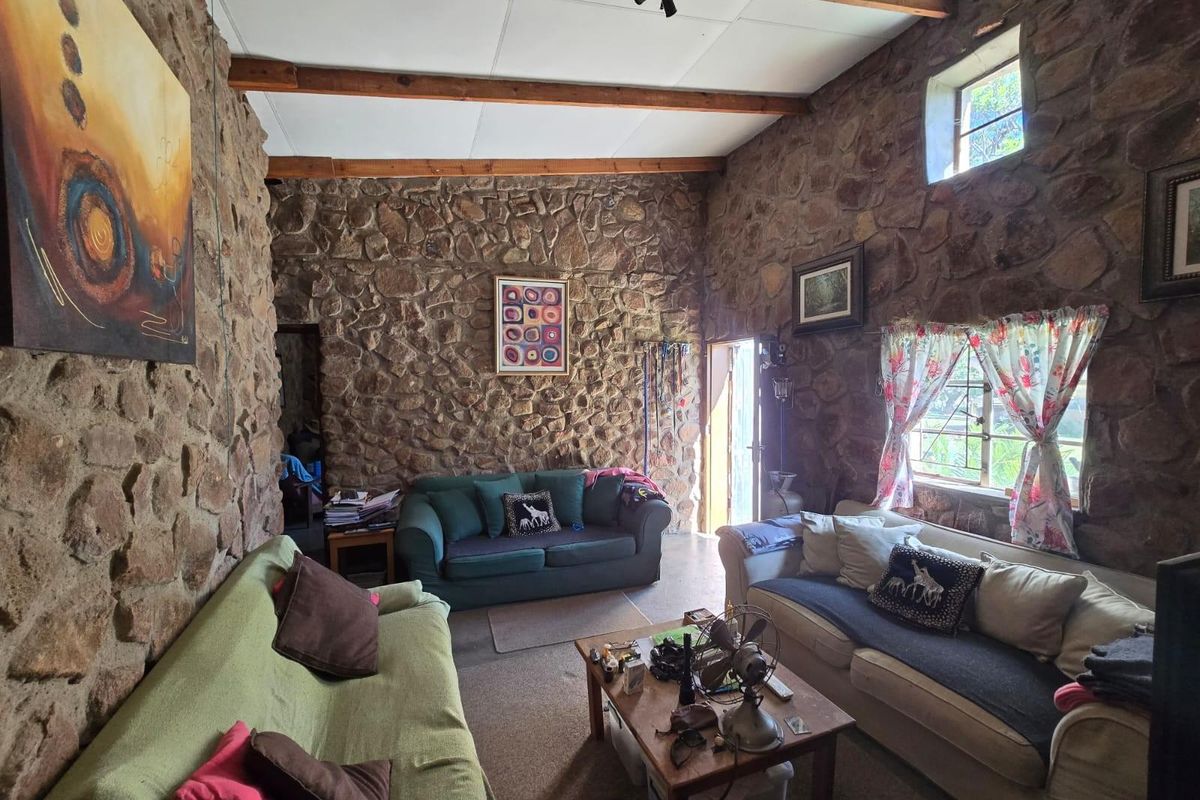 Rustic living room featuring exposed natural stone walls, high vaulted ceilings with timber beams, and large windows providing natural light.