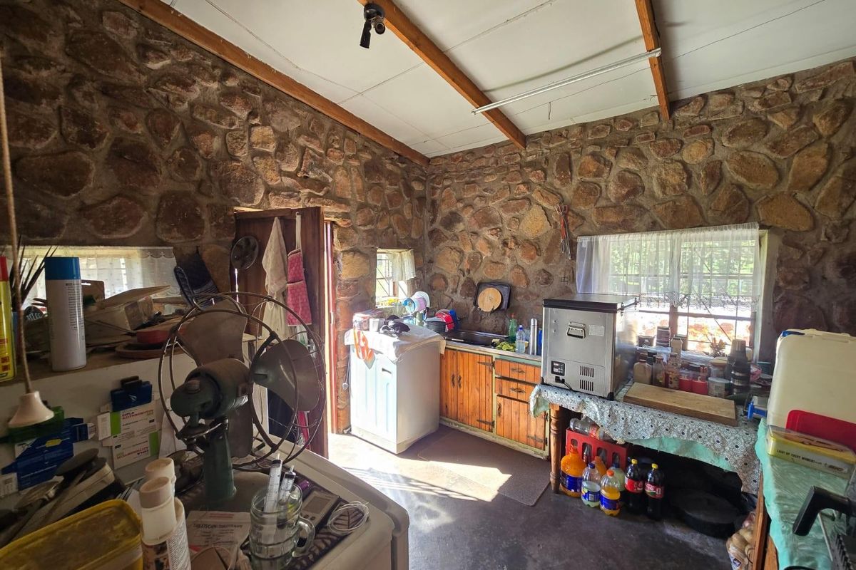 Rustic kitchen area featuring exposed natural stone walls, timber ceiling beams, and basic wooden cabinetry in a farm-style setting.