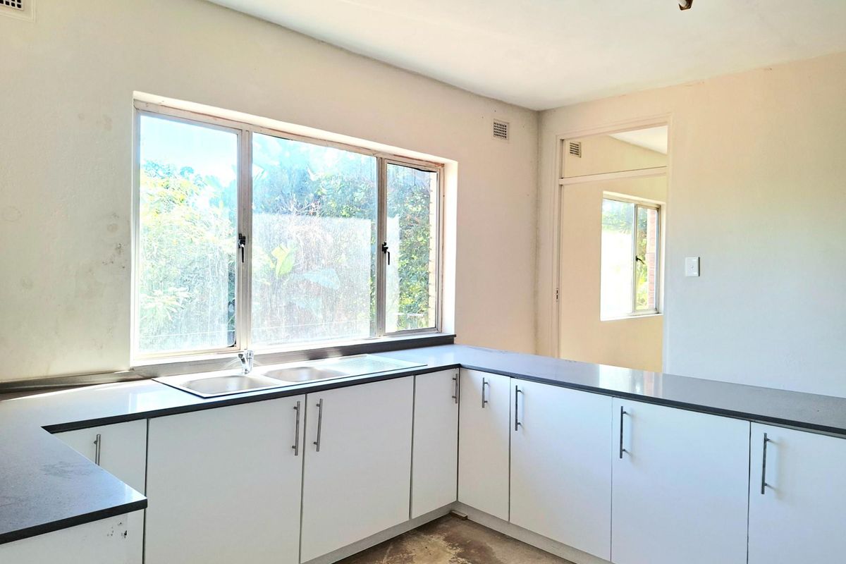A functional kitchen space featuring white cabinetry, dark countertops, and a double sink, awaiting final flooring installation and cosmetic updates.
