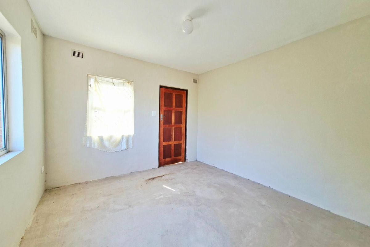 An empty bedroom featuring plain walls, a wooden door, and unfinished concrete flooring, offering a blank canvas for renovation.