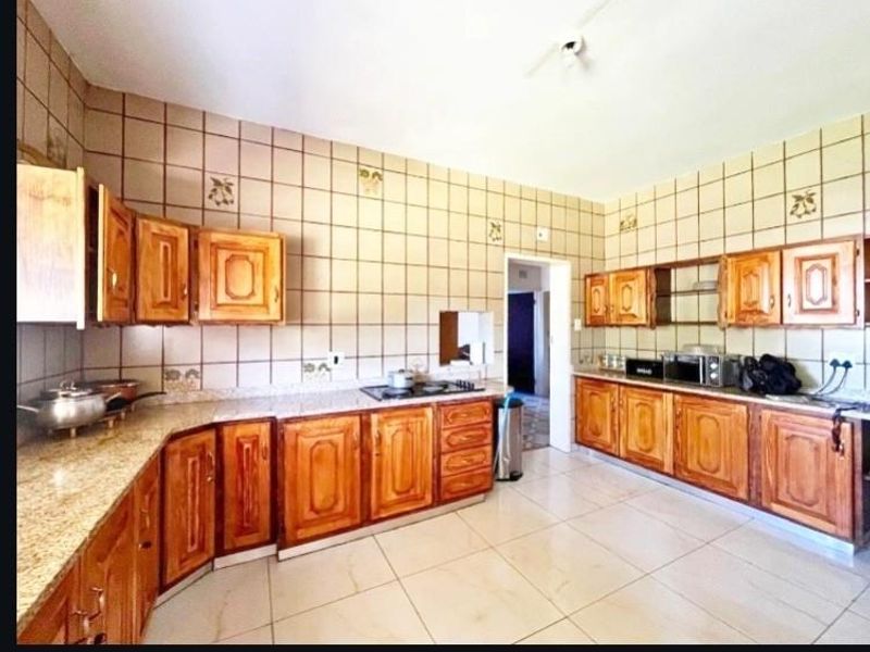 Spacious kitchen featuring extensive wooden cabinetry, granite countertops, and tiled splashbacks, offering a functional layout with ample storage and workspace.