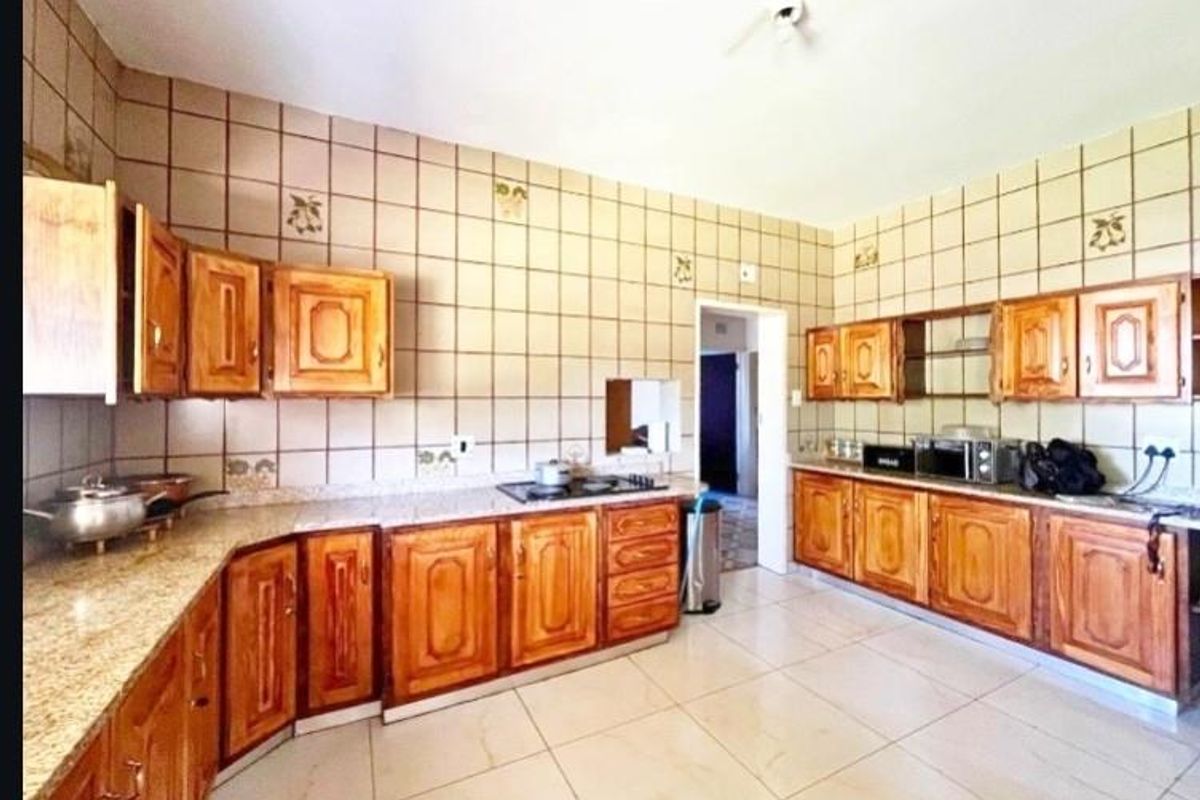 Spacious kitchen featuring extensive wooden cabinetry, granite countertops, and tiled splashbacks, offering a functional layout with ample storage and workspace.