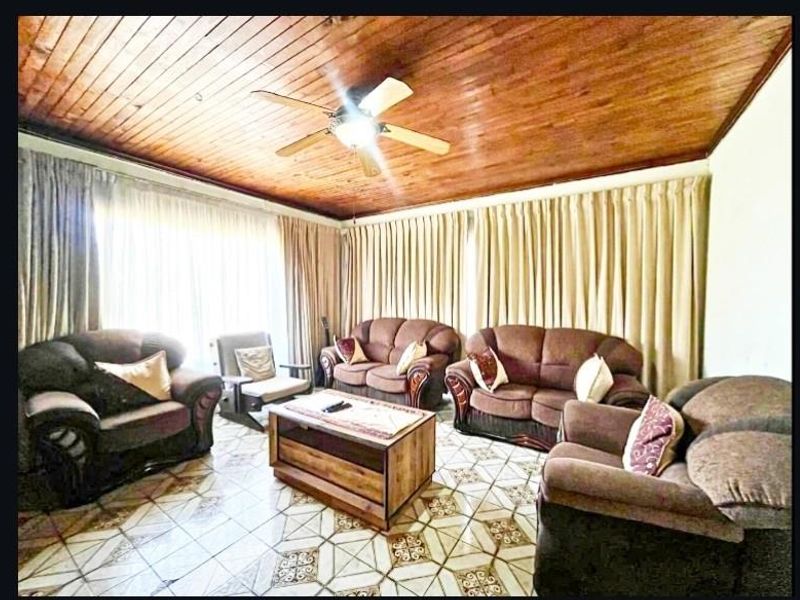 A living room featuring a timber-clad ceiling, ceiling fan, and patterned tiled flooring, offering a traditional aesthetic.