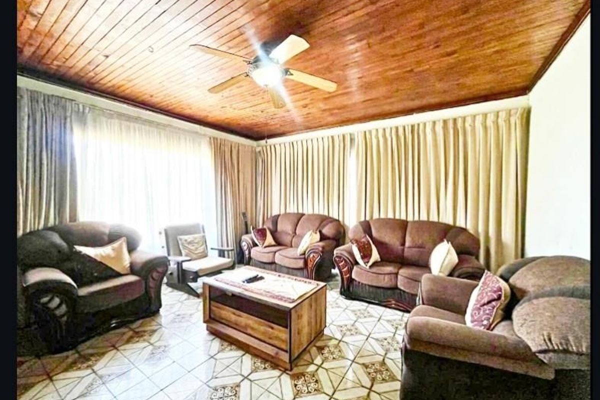 A living room featuring a timber-clad ceiling, ceiling fan, and patterned tiled flooring, offering a traditional aesthetic.