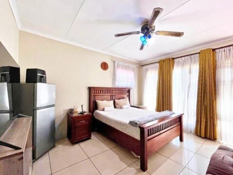 A bedroom featuring tiled flooring and a ceiling fan, with large windows allowing for natural light.