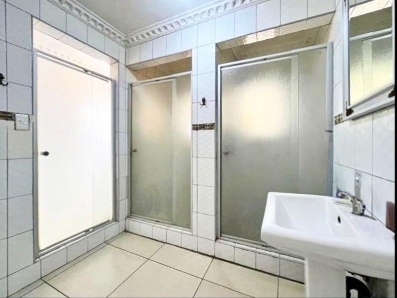 A functional bathroom featuring a pedestal basin and multiple shower cubicles with tiled finishes throughout.