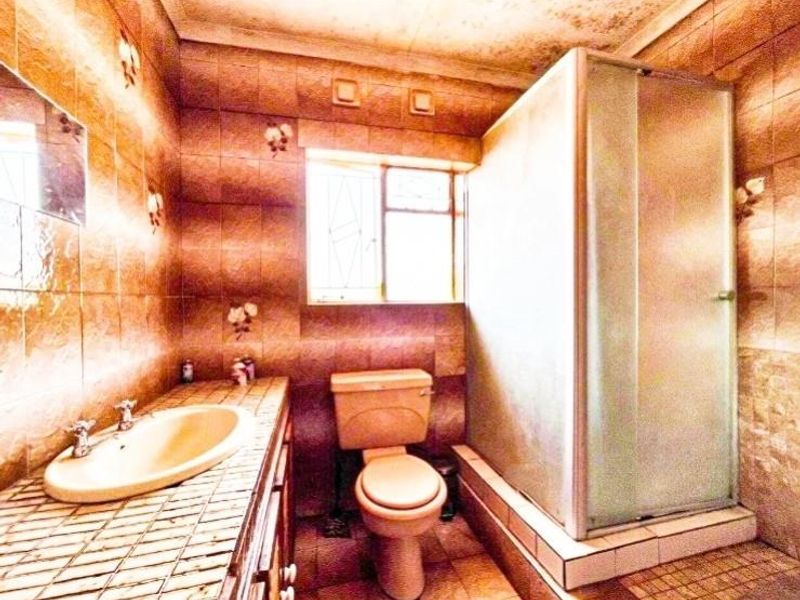 A dated bathroom featuring a shower enclosure, vanity basin, and toilet with tiled finishes throughout, requiring cosmetic updates to improve the overall aesthetic.