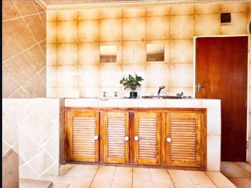 A dated bathroom featuring a double vanity with wooden cabinetry and tiled wall finishes, offering significant potential for a modern renovation.