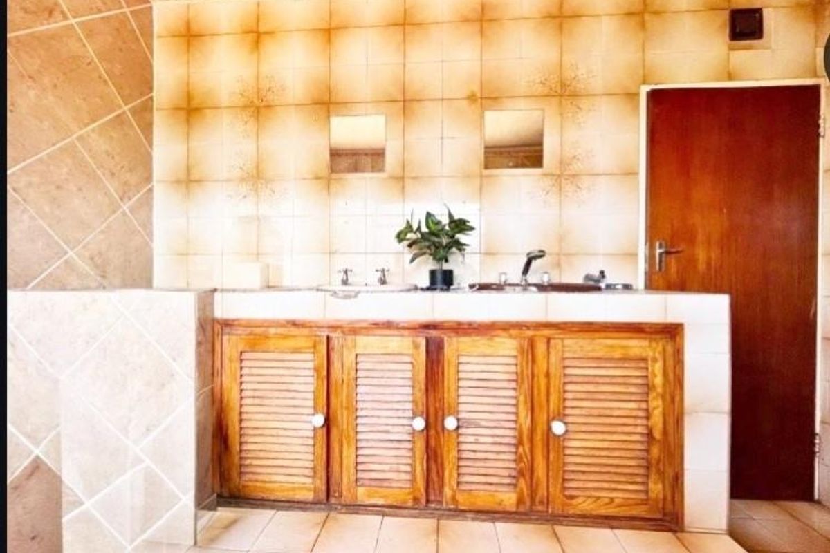 A dated bathroom featuring a double vanity with wooden cabinetry and tiled wall finishes, offering significant potential for a modern renovation.