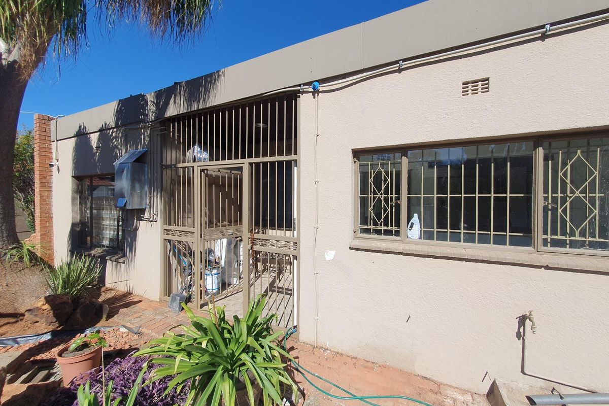 Rear exterior view of the property featuring a secure gated entrance, security bars on windows, and an external water tap.