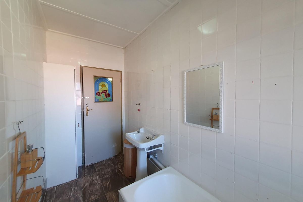 A dated bathroom featuring a pedestal sink, bathtub, and fully tiled walls. The space offers a functional layout ready for modern renovation.