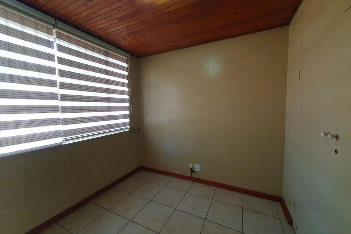 An empty bedroom featuring ceramic floor tiles, a timber-clad ceiling, and a built-in cupboard, offering a blank canvas for personalization.