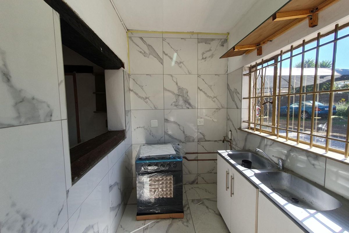 A compact kitchen featuring marble-look wall and floor tiles, a double stainless steel sink, and a new freestanding stove, currently in an unfinished state.