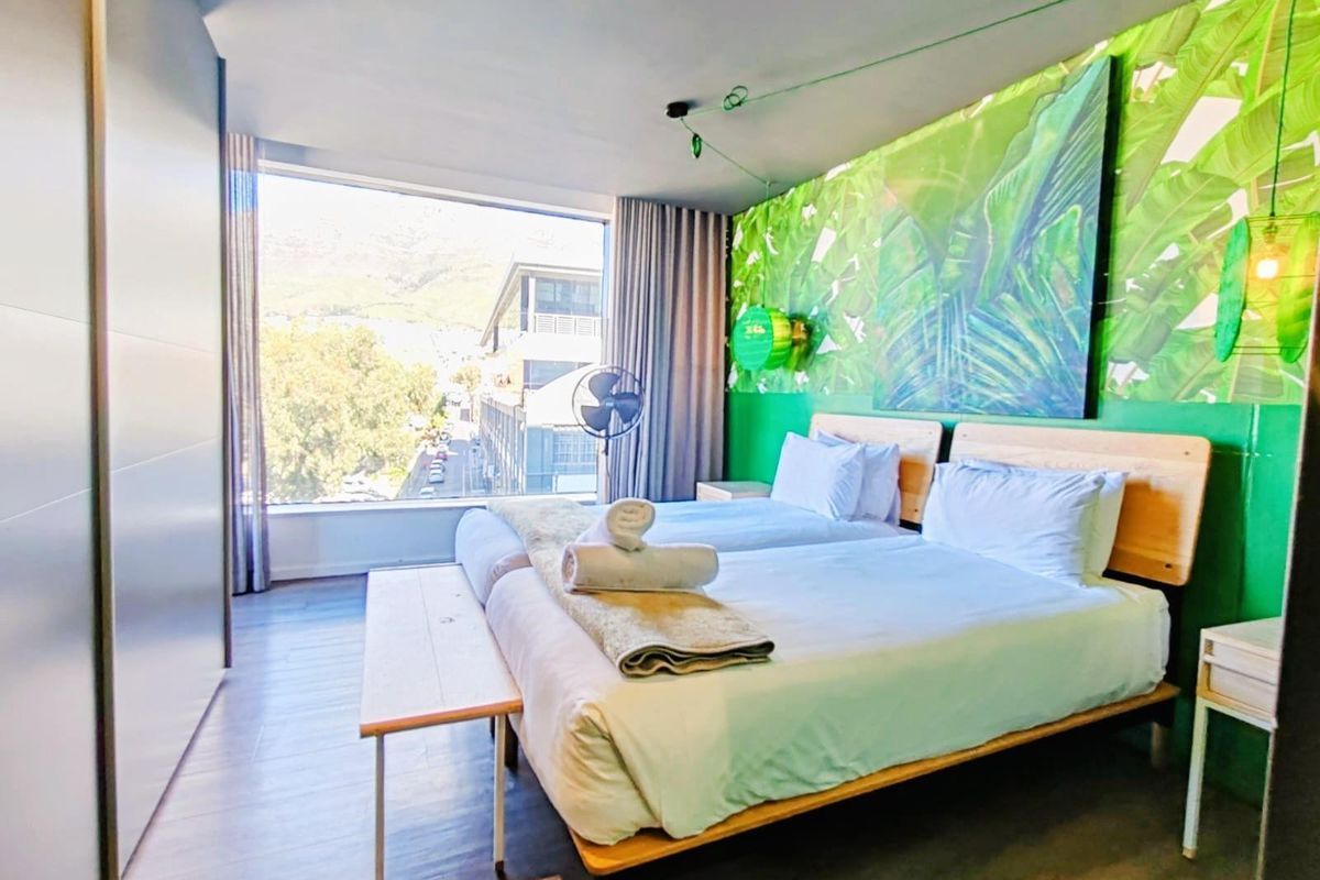 A modern bedroom featuring large floor-to-ceiling windows with urban views, built-in wardrobe, and a vibrant green accent wall.