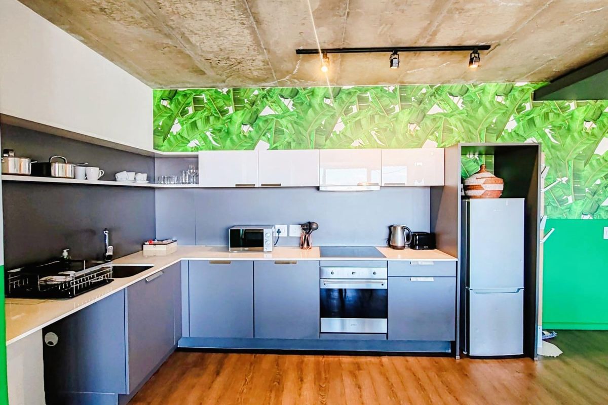 Modern kitchen featuring grey cabinetry, integrated oven and hob, exposed concrete ceiling, and vibrant botanical wallpaper accents.