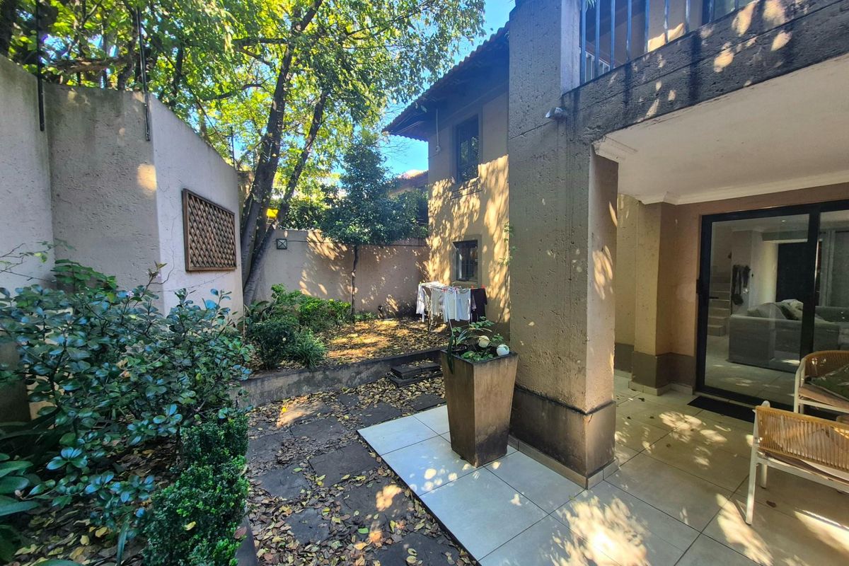 A private rear garden area featuring a paved patio, established trees, and direct access to the interior living space through sliding glass doors.