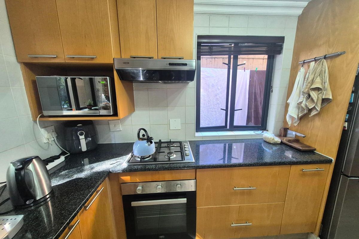 Compact kitchen featuring wooden cabinetry, granite countertops, a built-in oven, gas hob, and extractor fan with a window overlooking the exterior.
