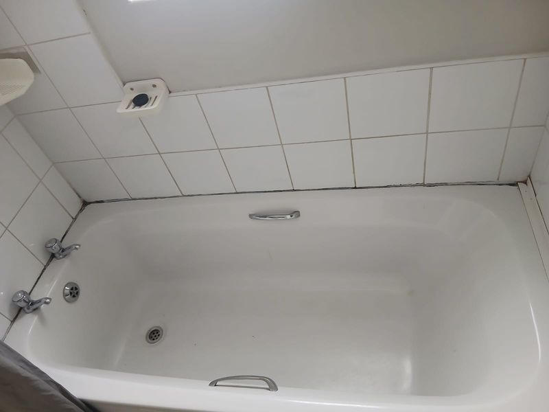 A standard bathroom bathtub featuring white ceramic wall tiles, chrome fixtures, and integrated grab handles, requiring minor maintenance to grout and sealant.