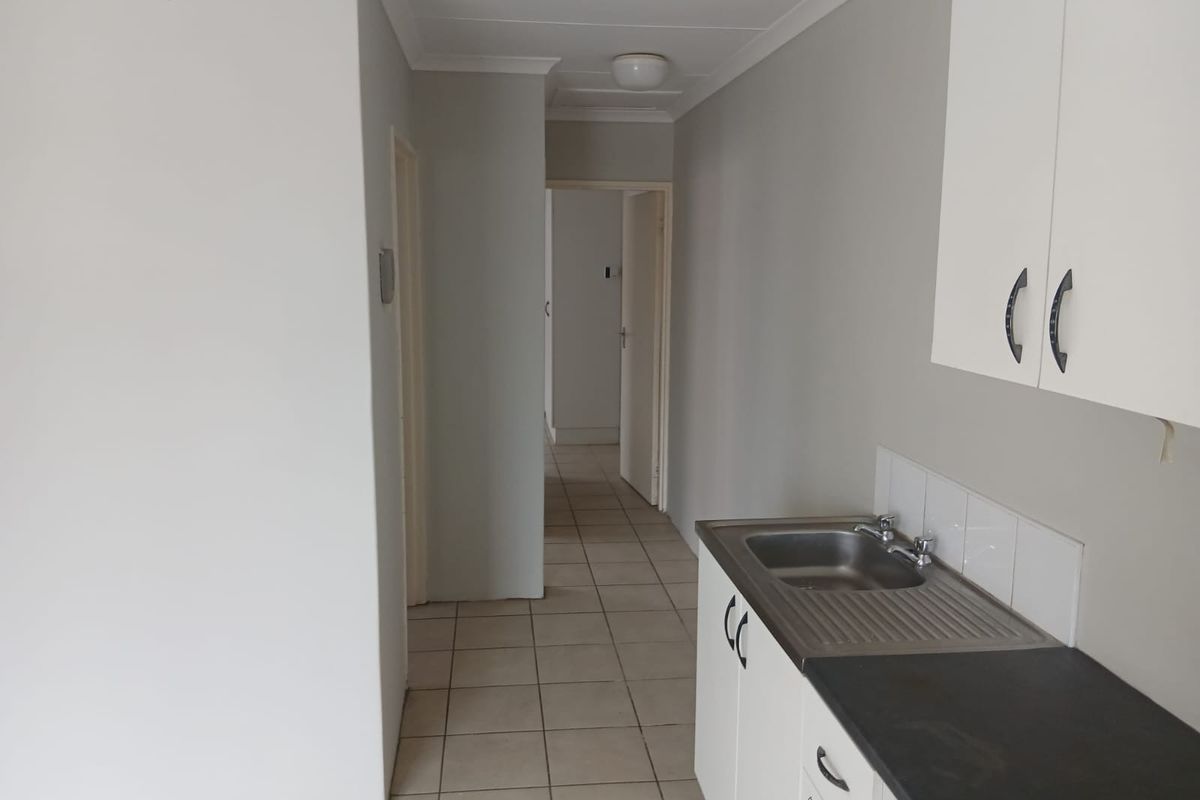 A functional scullery or utility area featuring built-in cabinetry, a stainless steel sink, and tiled flooring, providing practical workspace and storage.