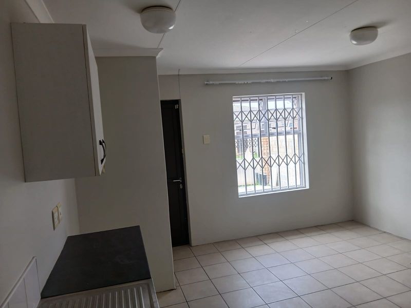 A clean, empty kitchen area featuring tiled flooring, built-in cabinetry, and a window fitted with a security gate.