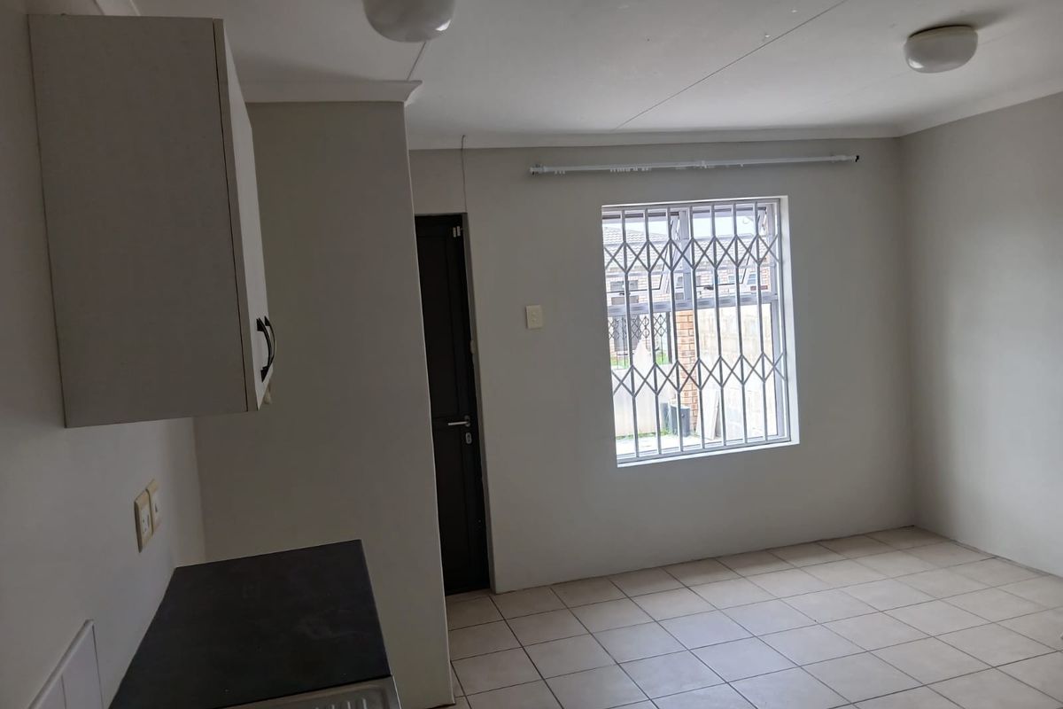 A clean, empty kitchen area featuring tiled flooring, built-in cabinetry, and a window fitted with a security gate.