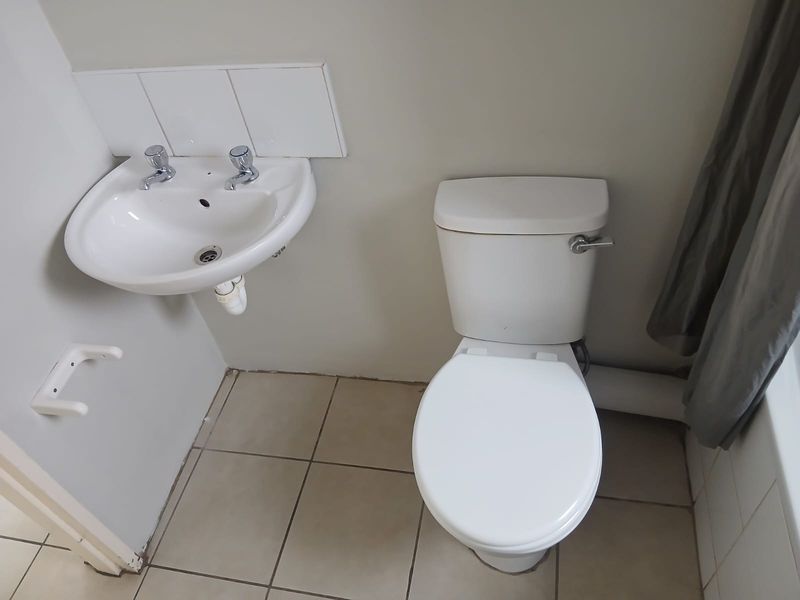 A functional bathroom featuring a wall-mounted basin, standard toilet, and tiled flooring, presenting a clean but dated aesthetic.