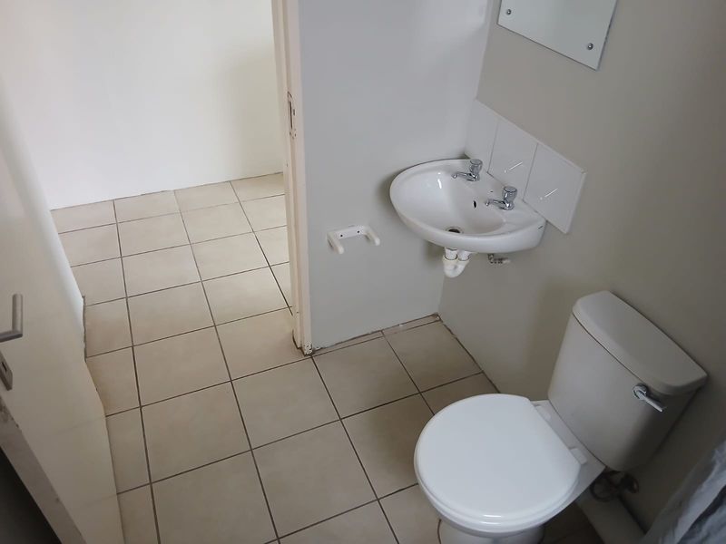 A compact, functional bathroom featuring a wall-mounted basin, toilet, and neutral tiled flooring.