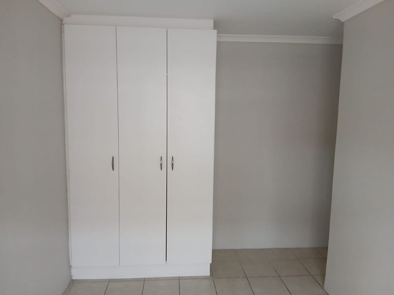 A clean, empty bedroom featuring neutral wall paint, tiled flooring, and white built-in cupboards with modern hardware.