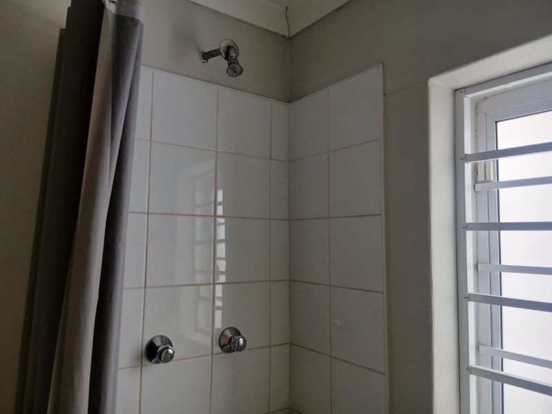 A functional shower area featuring white wall tiles, a standard shower head, and a window with security bars.