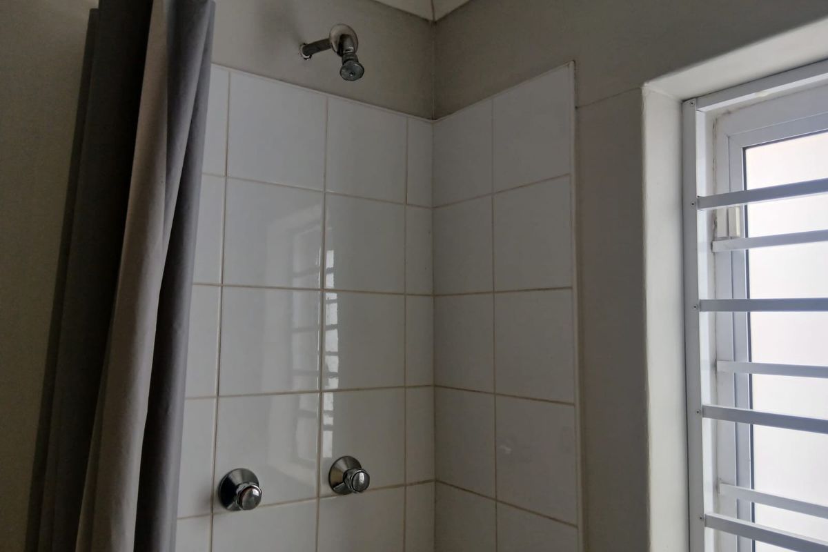 A functional shower area featuring white wall tiles, a standard shower head, and a window with security bars.