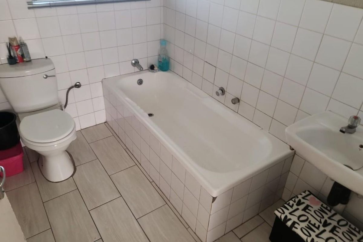 A functional bathroom featuring a standard bathtub, pedestal basin, and toilet with tiled walls and flooring.