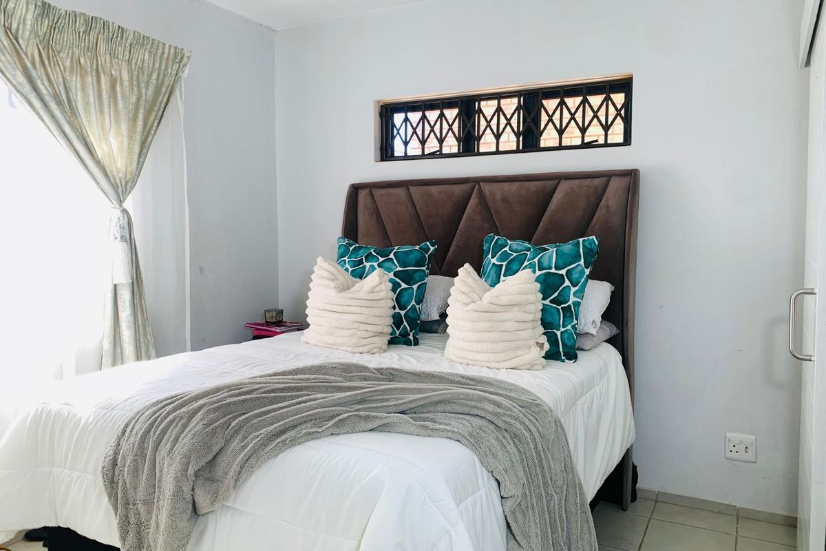 A bedroom featuring tiled flooring and a high-level window with security bars.