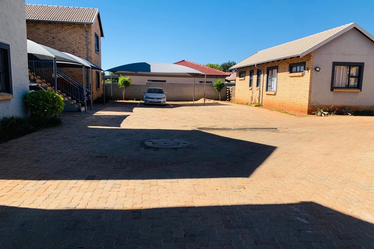 A paved courtyard area between apartment buildings featuring covered parking bays and brick exterior facades.