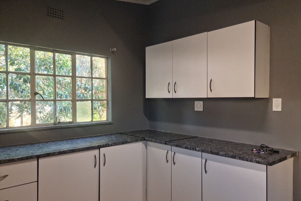A functional kitchen area featuring white cabinetry, dark laminate countertops, and a window providing natural light.