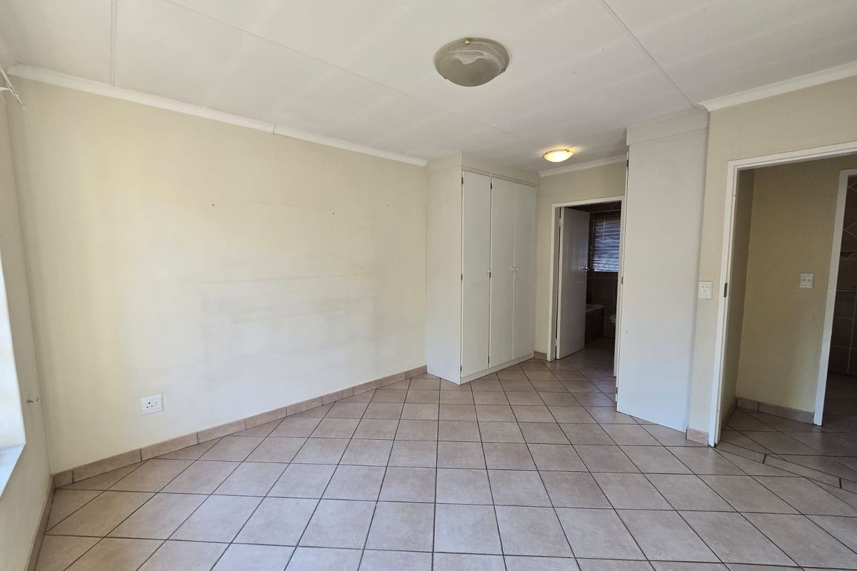 A vacant bedroom featuring neutral tiled flooring, built-in cupboards, and access to an adjoining bathroom.