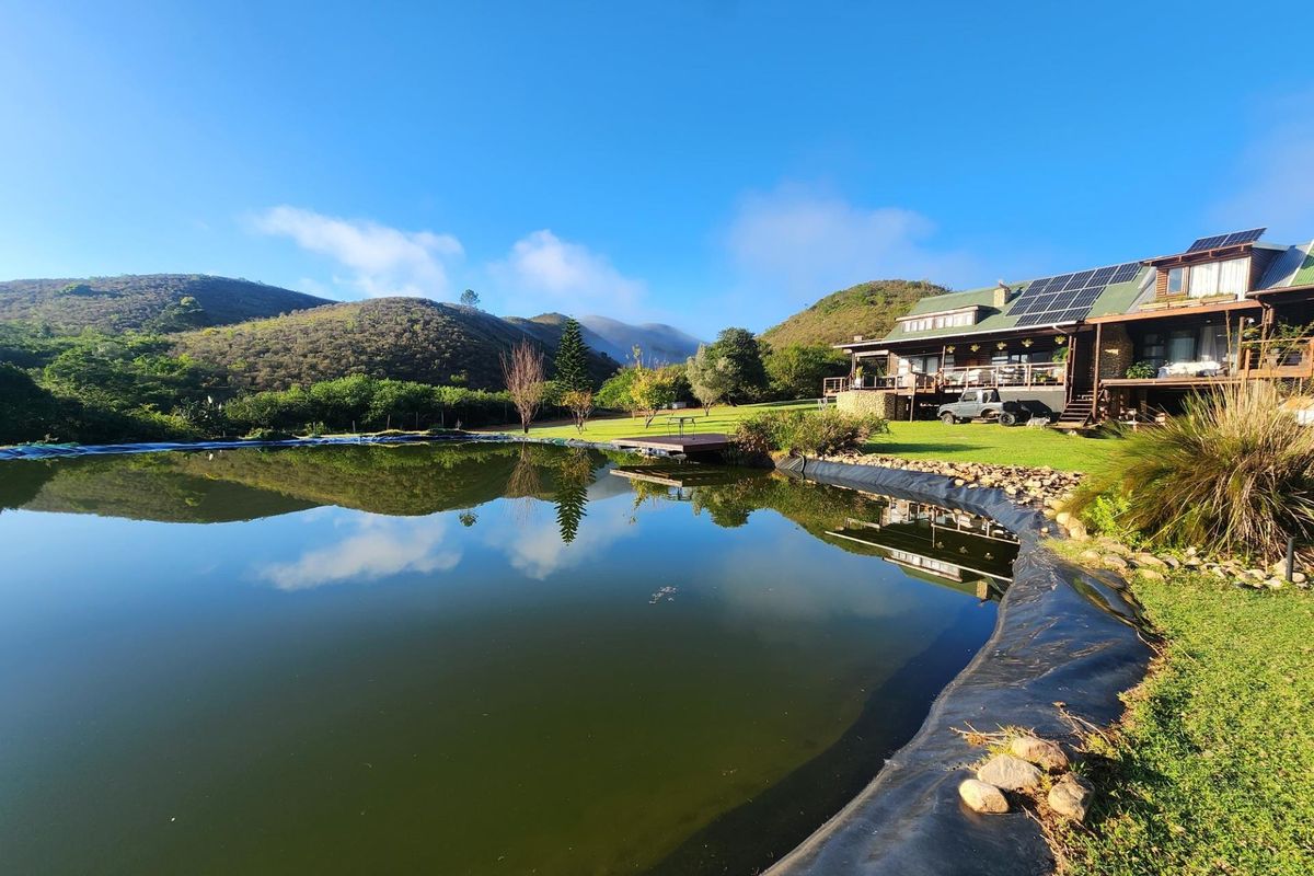 A scenic view of a farm property featuring a large dam, landscaped lawn, and a multi-level house with solar panels and timber decking.