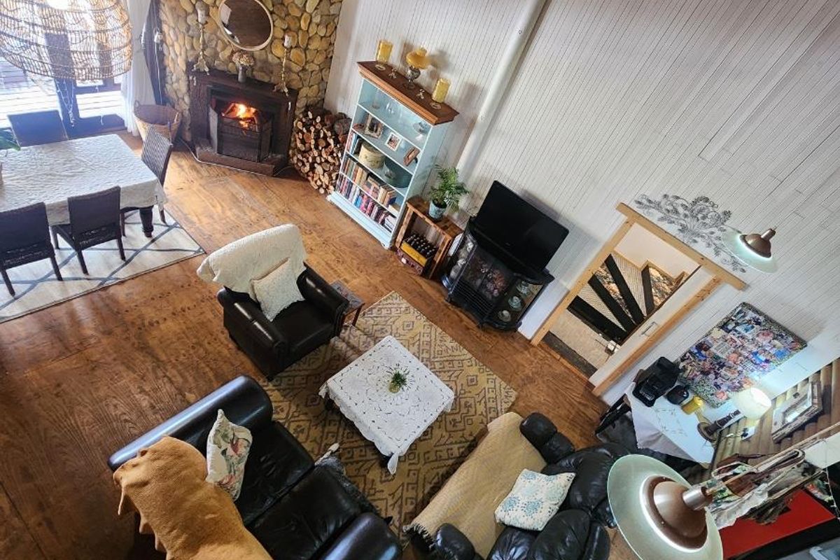 Spacious living area featuring a prominent stone fireplace, high vaulted ceilings with exposed timber beams, and warm hardwood flooring in a rustic farm setting.