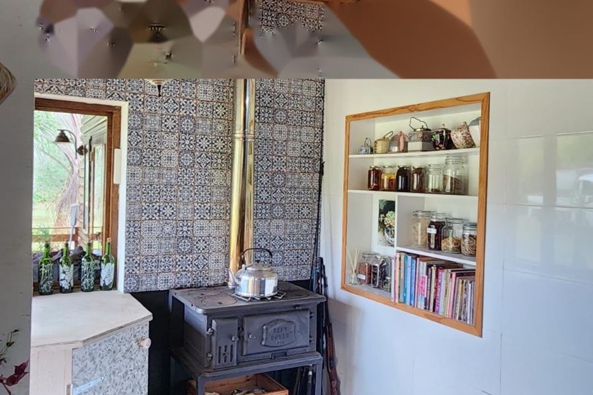 Rustic kitchen area featuring a vintage cast iron wood-burning stove, decorative patterned wall tiles, and built-in shelving with exposed timber ceiling beams.