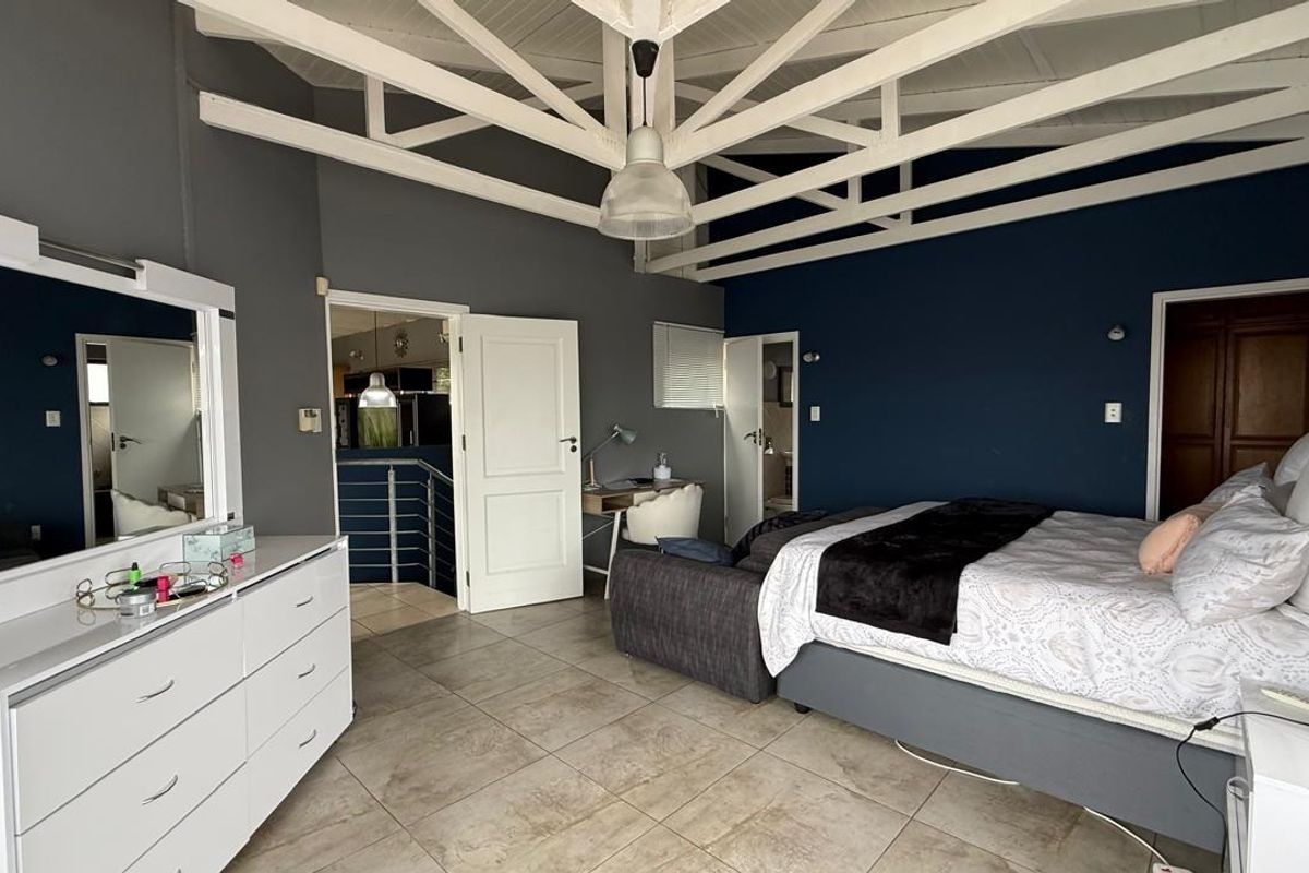 Spacious bedroom featuring high vaulted ceilings with exposed white trusses, tiled flooring, and direct access to an adjoining room.