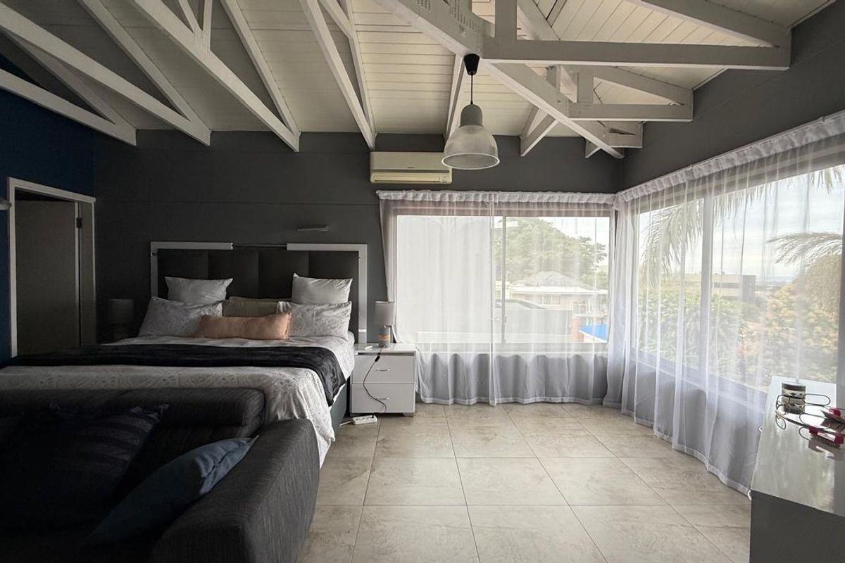 Spacious bedroom featuring vaulted exposed beam ceilings, large windows with natural light, tiled flooring, and a wall-mounted air conditioning unit.