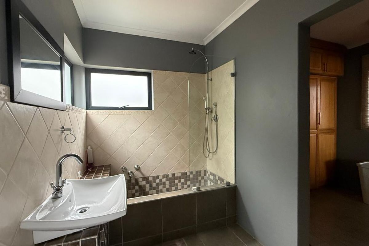 A functional bathroom featuring a shower-over-bath combination, a modern vessel sink, and neutral tiled finishes with grey wall accents.