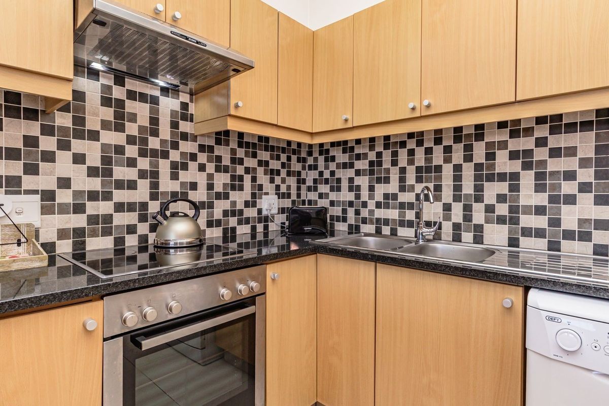 A functional kitchen featuring light wood cabinetry, a black granite countertop, a stainless steel oven, an extractor fan, and a mosaic tile backsplash.