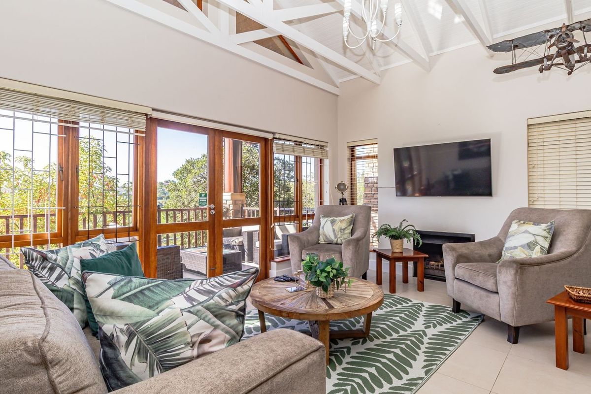 Spacious living room featuring vaulted ceilings with exposed beams, tiled flooring, and large wooden framed glass doors leading to an outdoor balcony.