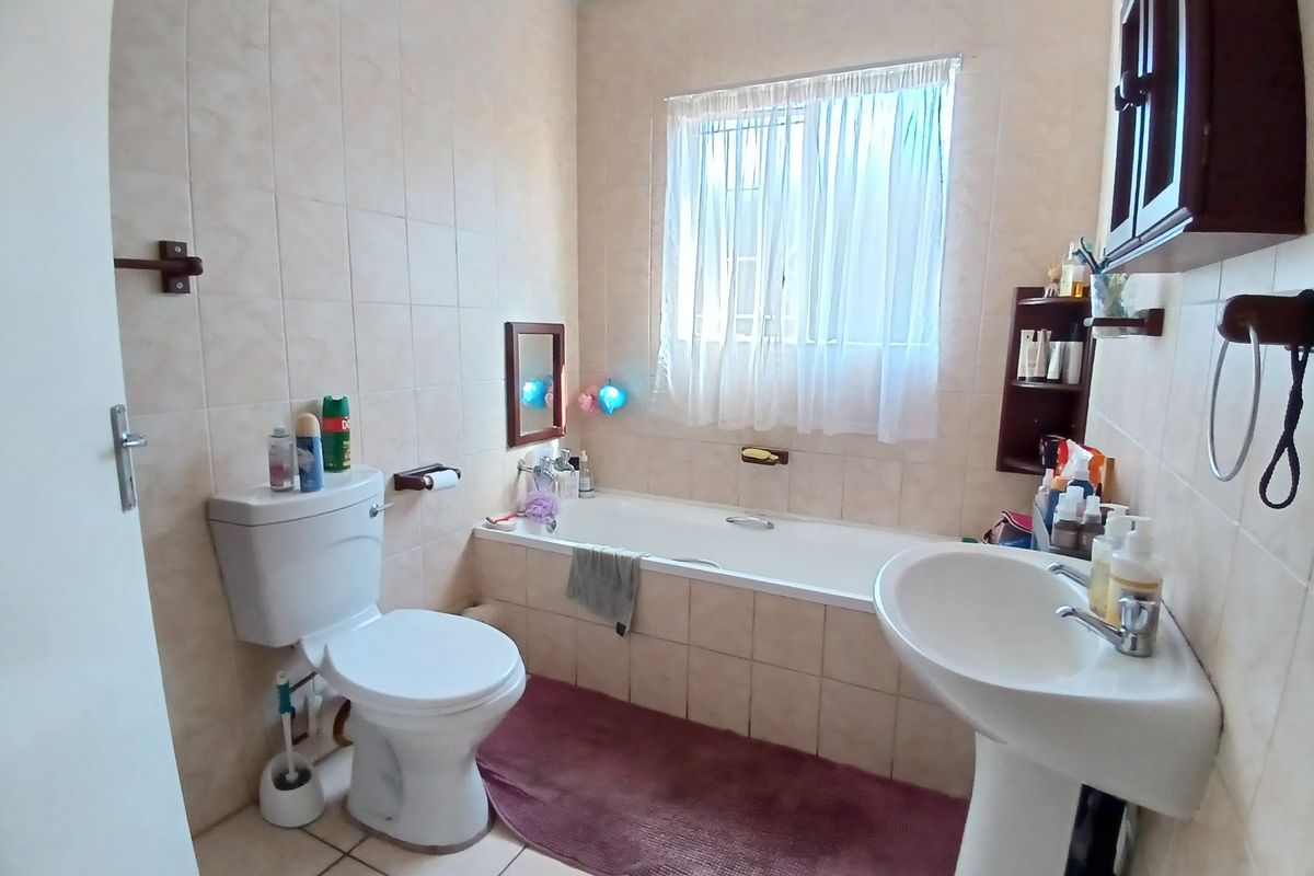 A functional bathroom featuring a pedestal basin, built-in bathtub, and toilet with neutral wall and floor tiling.