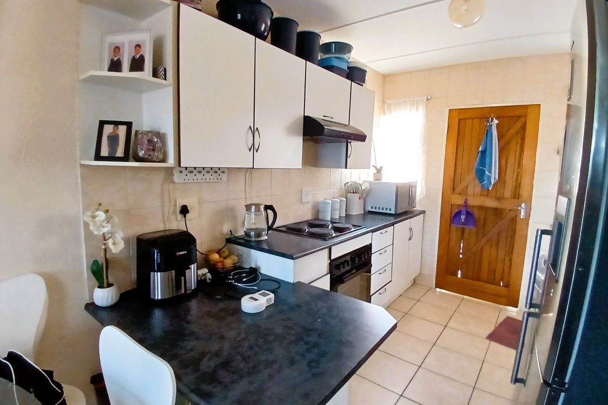 A functional kitchen featuring built-in cabinetry, laminate countertops, an electric hob with extractor fan, and tiled flooring, providing a practical workspace for daily cooking.