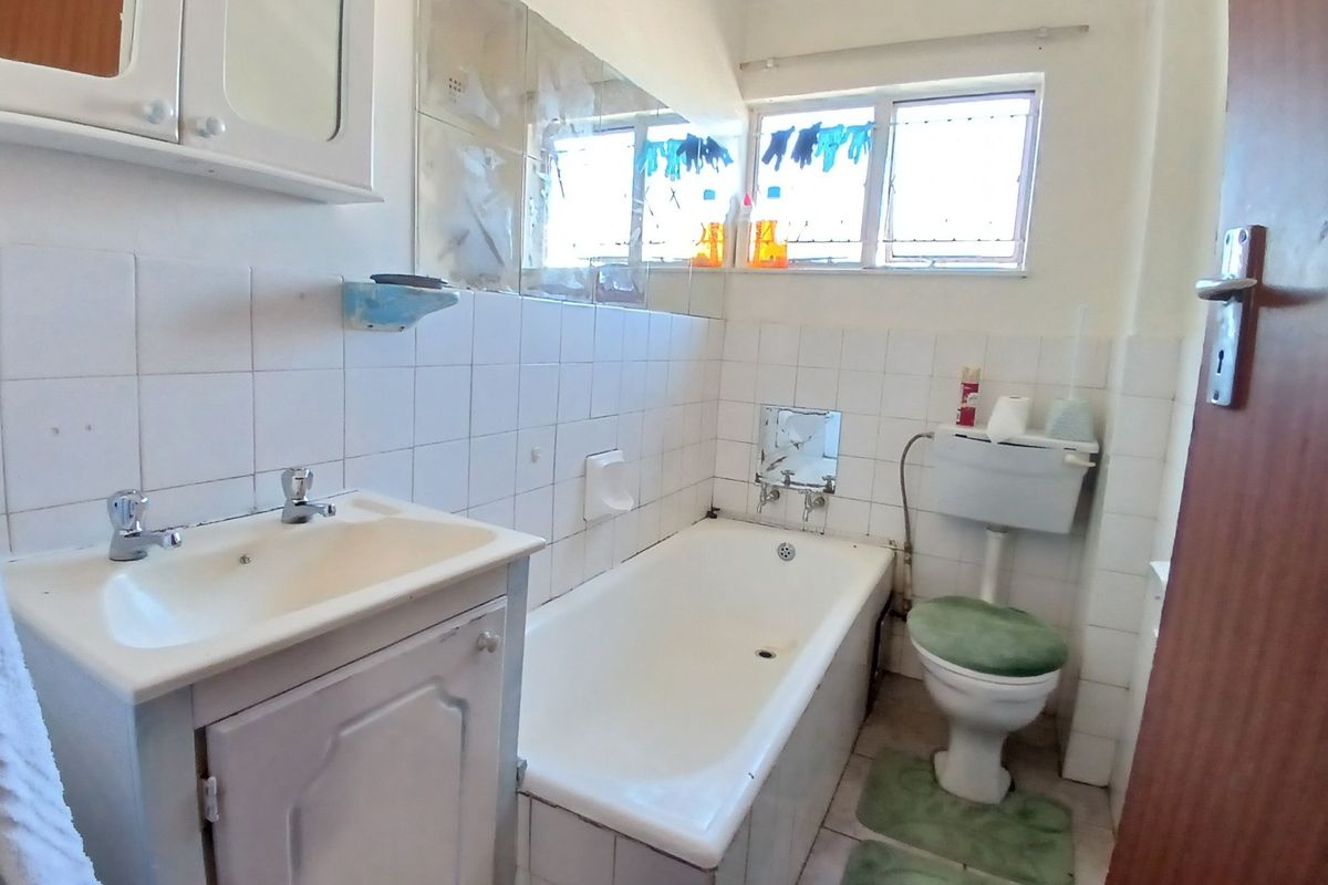 A functional bathroom featuring a standard bathtub, vanity basin, and toilet with tiled walls and natural light from a window.