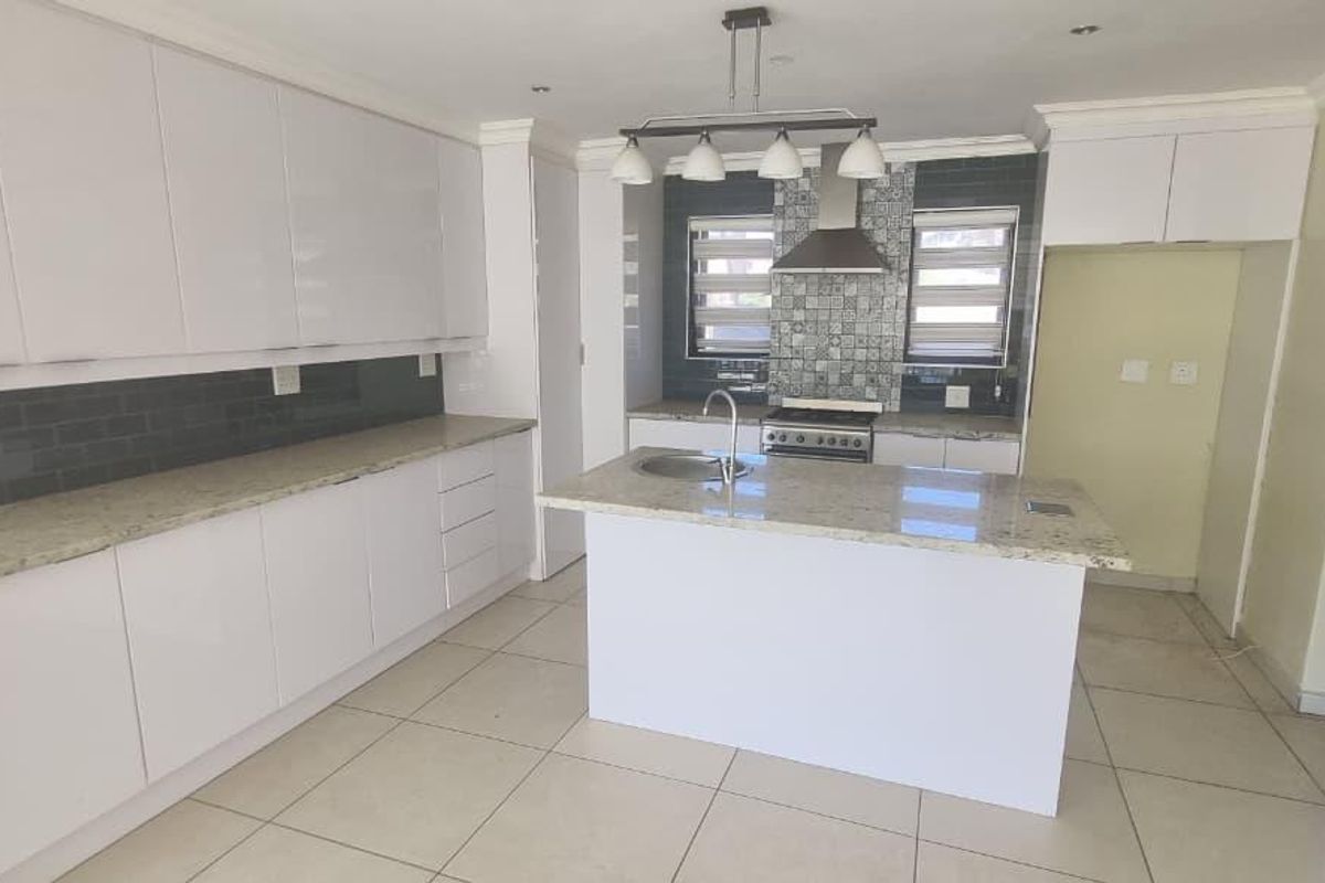 Modern kitchen featuring white cabinetry, granite countertops, a central island with a prep sink, and a tiled backsplash with a stainless steel extractor fan.